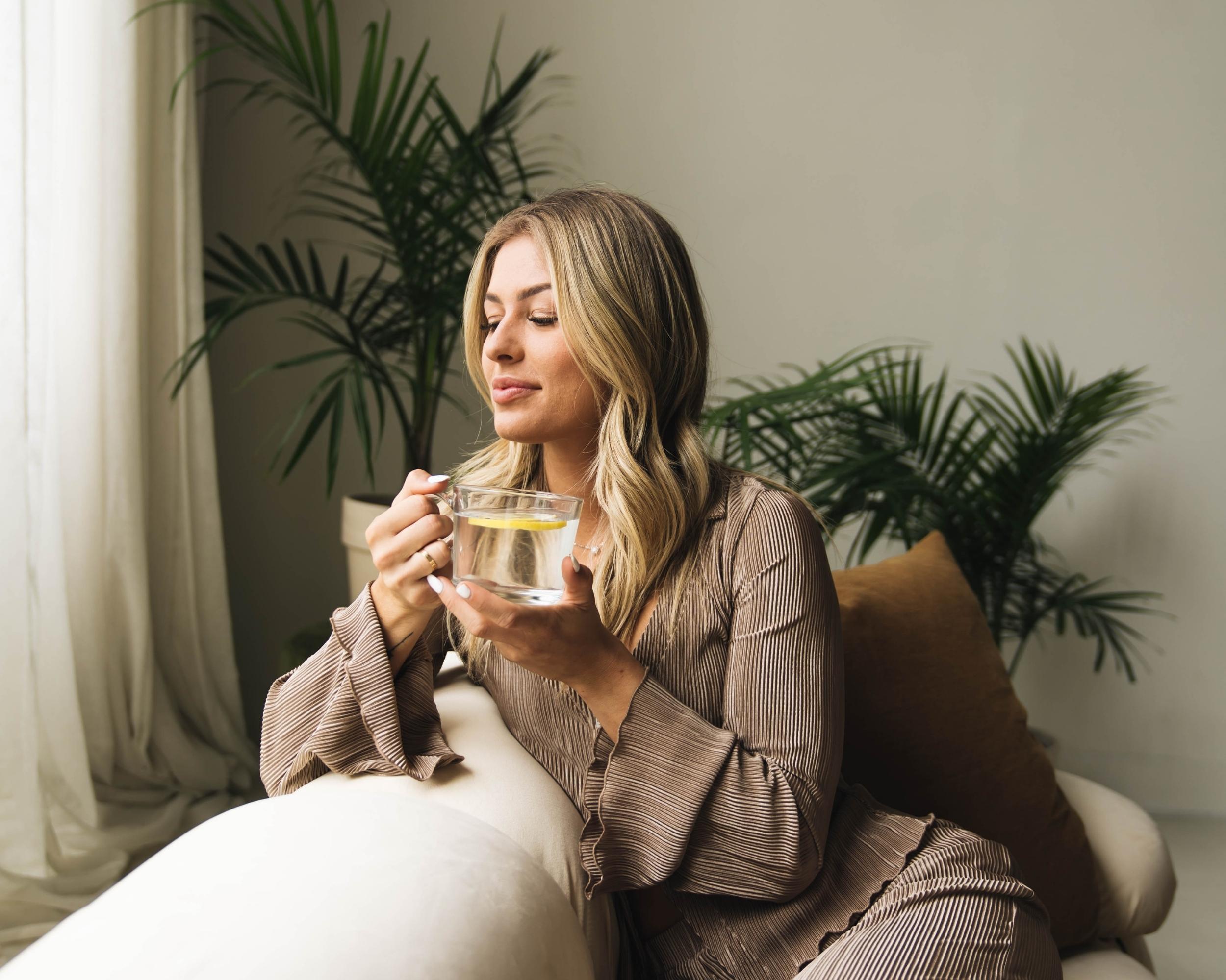 Woman drinking hot lemon water on couch 