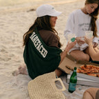Jordan Harper eating pizza on a beach wearing Barefaced Varsity Crewneck sweatshirt