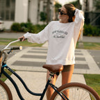 Woman wearing No Sun Club Crewneck sweatshirt riding a bike